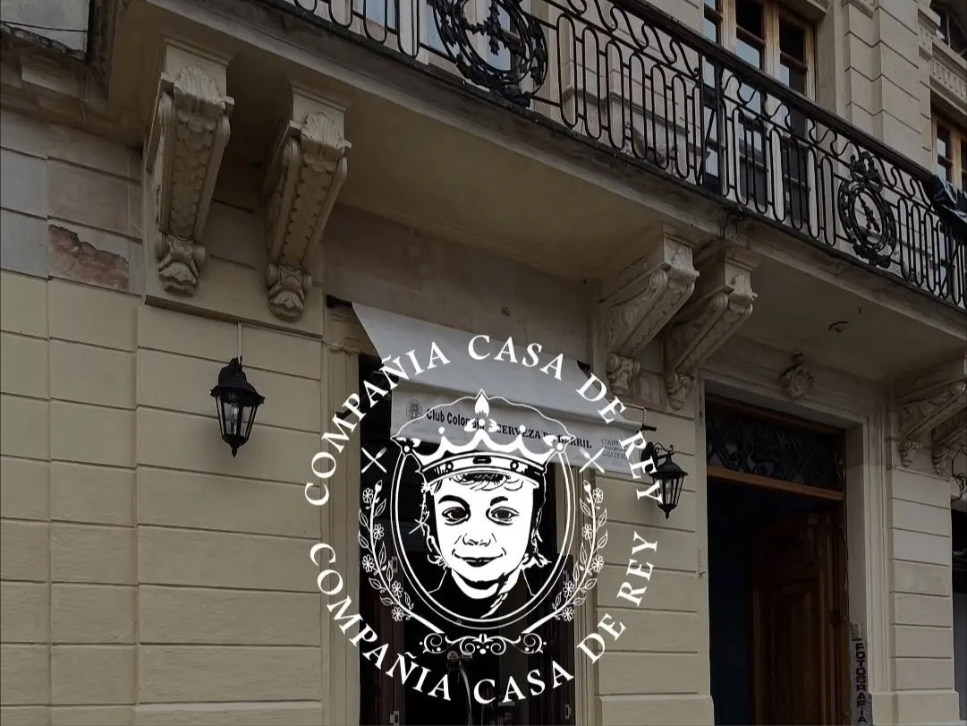 Fachada de estilo clásico con detalles ornamentales, balcón de hierro forjado y entrada de madera, identificada con el emblema de la compañía.