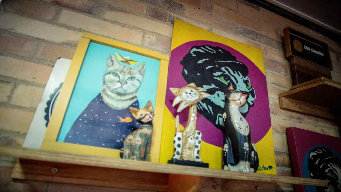 Estantería de madera sobre pared de ladrillo exhibiendo diversas piezas de arte y figuras decorativas de temática felina.