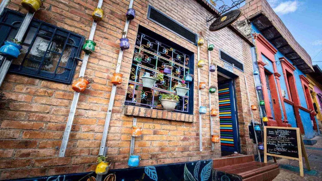 Fachada de ladrillo decorada con jarras de colores, reja de ventana artesanal, puerta abierta y pizarra con menú.
