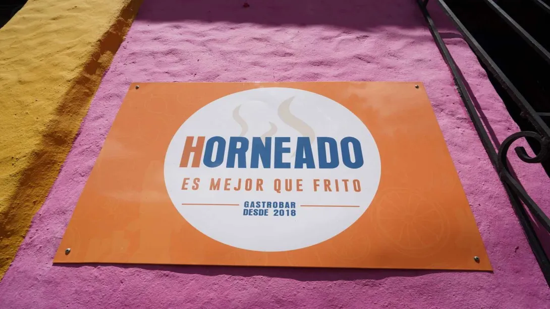 Letrero naranja sobre pared rosa que destaca el método de cocción principal del gastrobar.