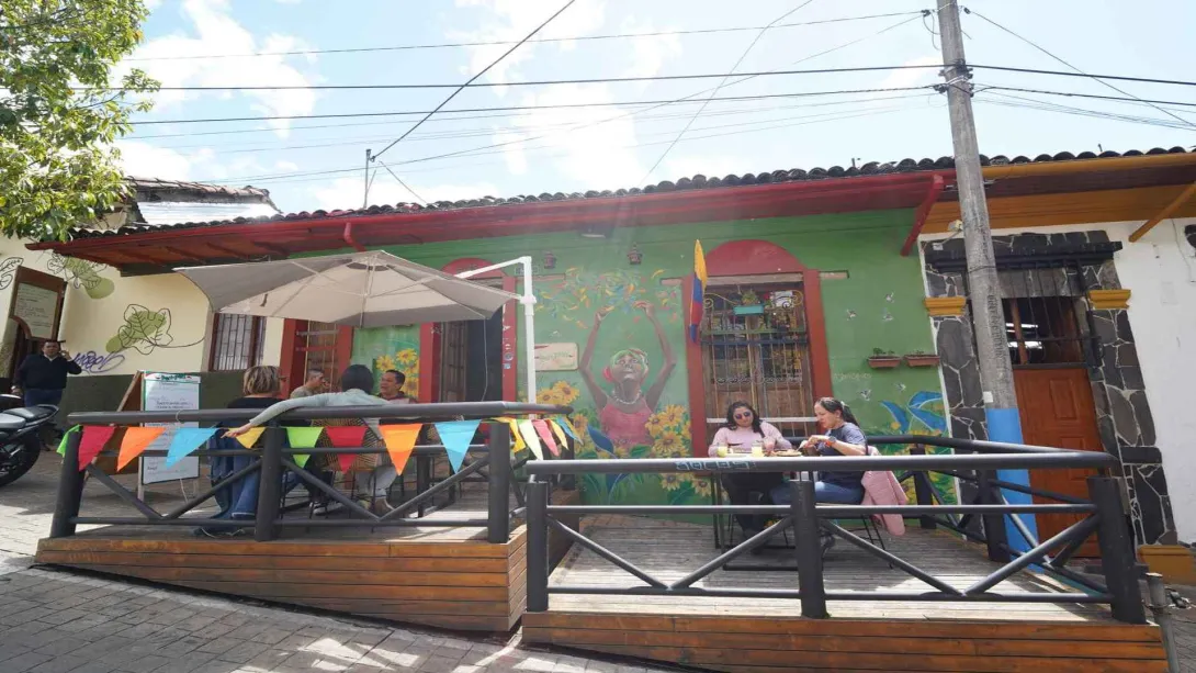 Fachada colorida del restaurante Peri Peri con terraza de madera, banderines y comensales al aire libre. 