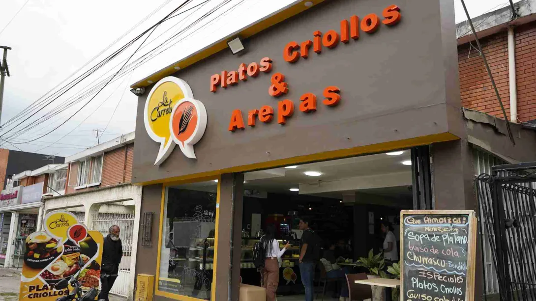  Fachada del restaurante La Garreta Platos Criollos & Arepas con tablero de menú ejecutivo en la entrada. 
