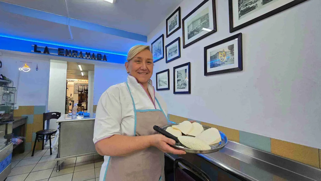Repostera sonriente sosteniendo bandeja con trozos de queso fresco en el interior del local. 