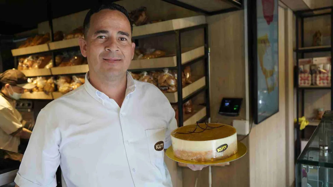 Hombre sonriente con camisa blanca sosteniendo una torta de maracuyá en la panadería Kuty. 