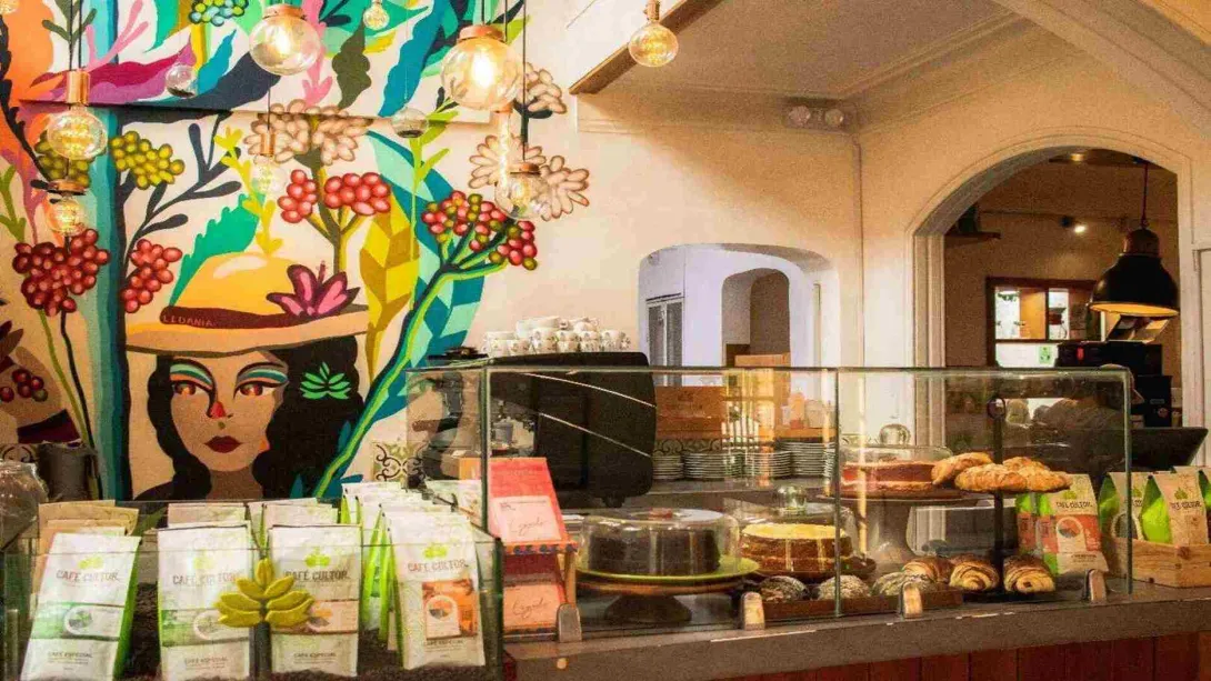  Mostrador con bolsas de café, vitrina de repostería y un colorido mural ilustrado con el rostro de una mujer. 