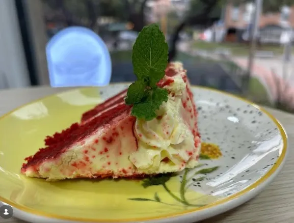 Porción de torta de frutos rojos con crema y hierbabuena.