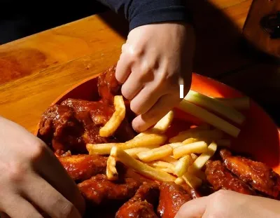 Alitas de pollo bañadas en salsa, acompañadas de papas fritas y vegetales.