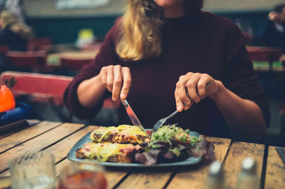 Comensal disfrutando un plato en un restaurante, acompañado de ensalada y otros alimentos.
