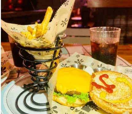 Hamburguesa con queso, lechuga y salsa, acompañada de papas fritas y una bebida gaseosa.