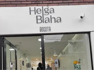 Fachada de la pastelería Helga Blaha en Bogotá, con letrero metálico sobre fondo blanco y amplios ventanales que permiten ver el interior del establecimiento.