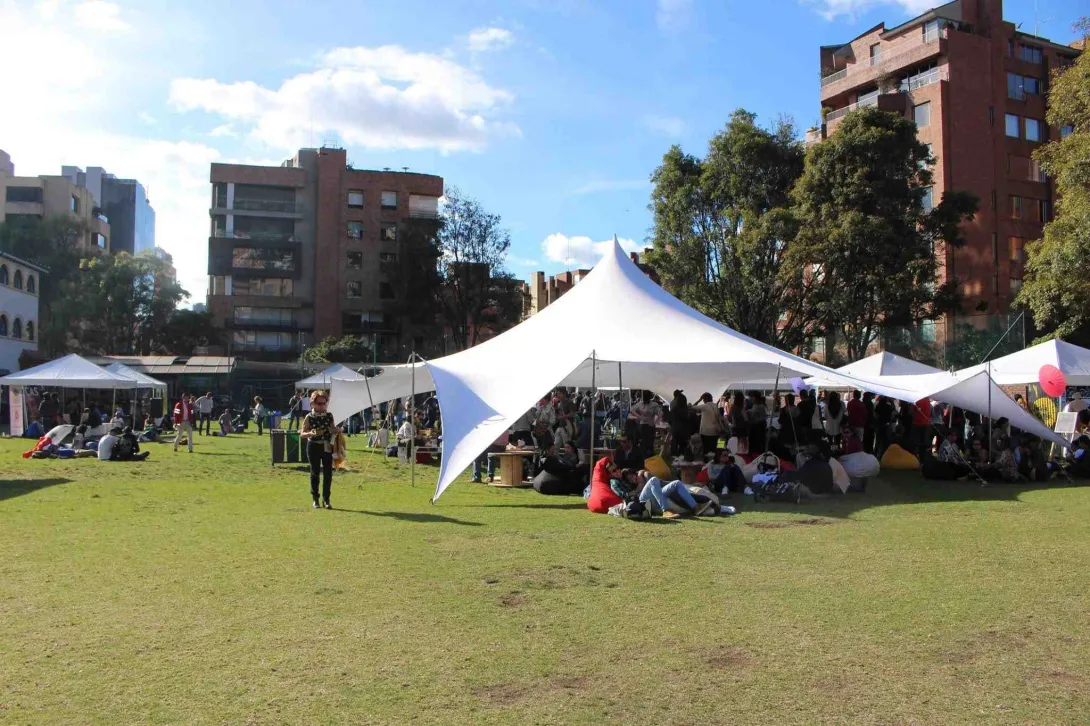 Personas disfrutando de un evento al aire libre en un parque, bajo grandes carpas blancas.