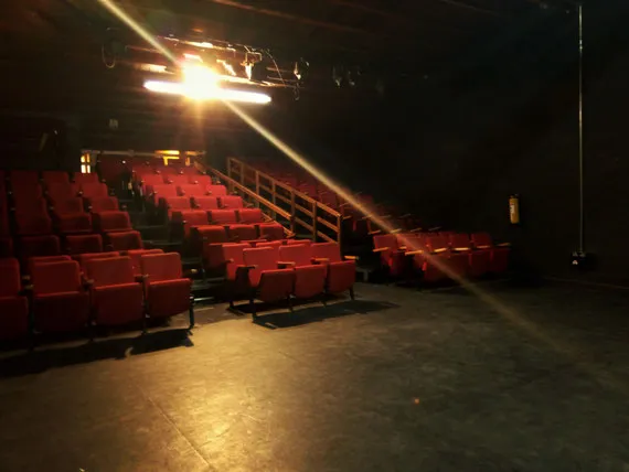 Sala de teatro con filas de sillas rojas, iluminación escénica y espacio dispuesto para disfrutar de una función.
