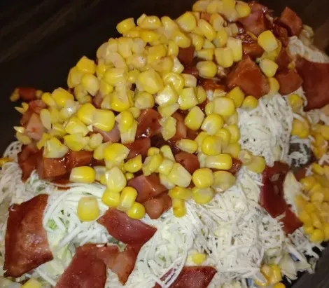 Salchipapa con salchicha, maíz dulce, queso rallado y salsas.