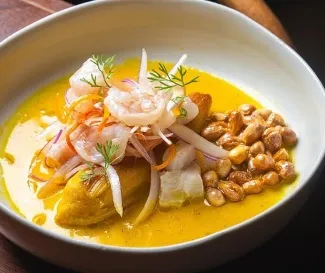 Plato de cocina peruana con pescado y camarones, acompañado de cebolla, ají, hierbas frescas y maíz tostado.
