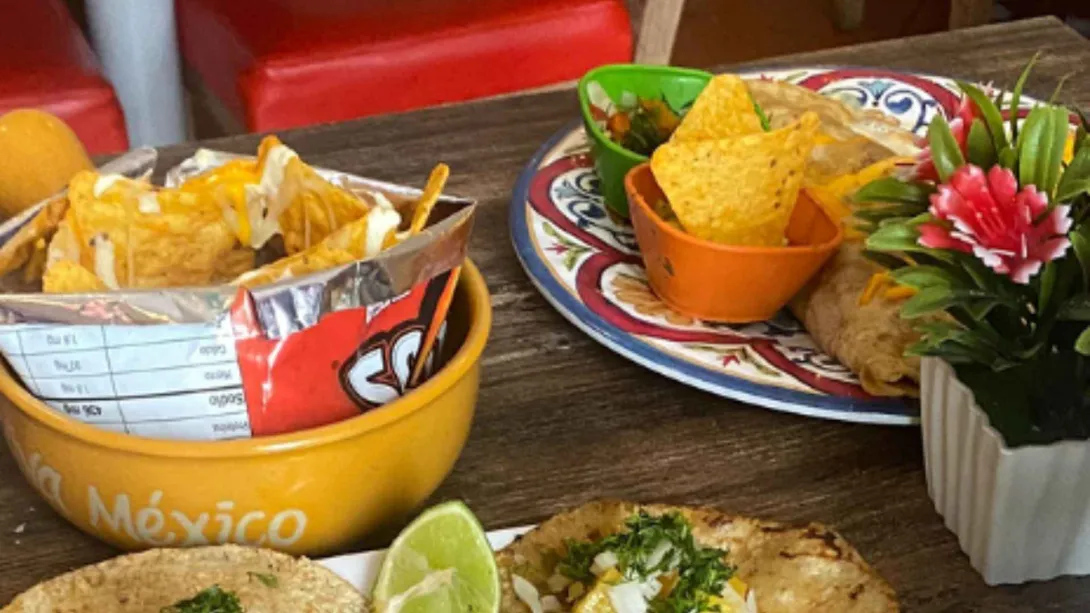 Platos de comida mexicana con nachos crujientes, tacos de maíz y burrito servidos en una mesa de madera de restaurante.   