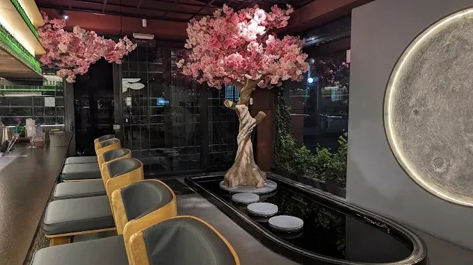 Interior de Gogi con barra, mesas de madera, árbol ornamental de flores rosadas y elementos decorativos de inspiración asiática.