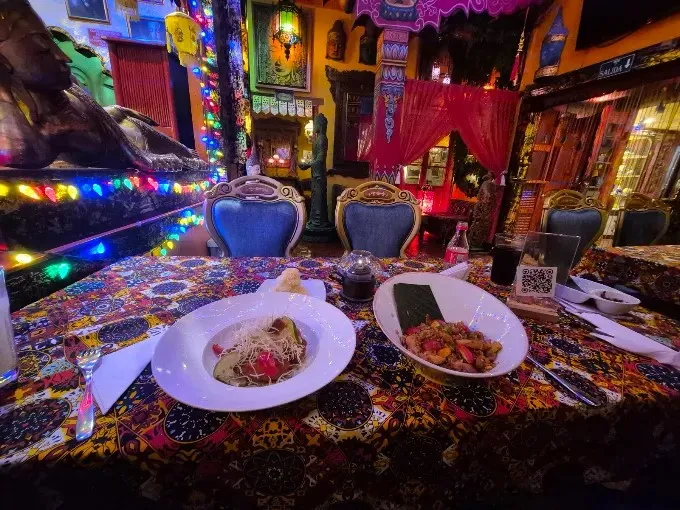 Mesa de Kathmandu con decoración oriental, manteles coloridos y platos de comida acompañados de bebidas.