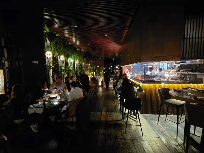 Interior de Salvaje Bogotá con comedor, barra de sushi a la vista, iluminación tenue y decoración con abundante vegetación.