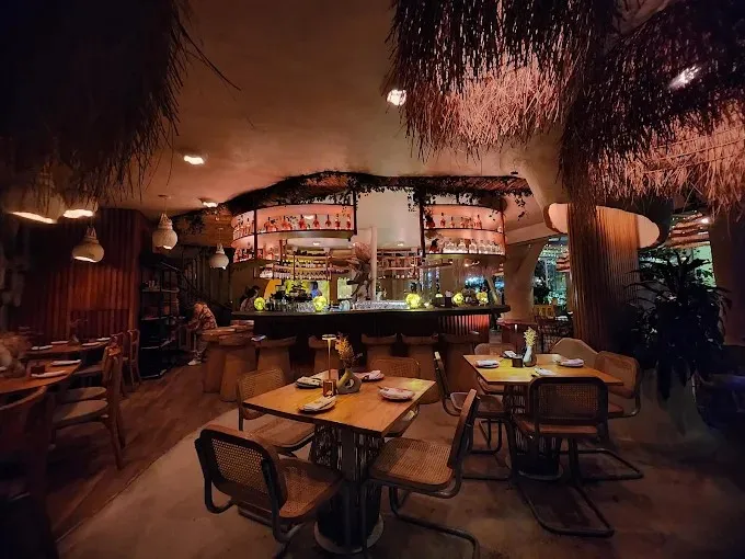 Interior de El Mono Bandido con barra central, iluminación cálida, decoración tropical y mesas para compartir.