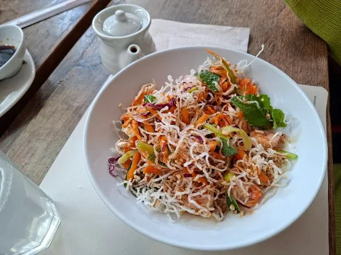 Plato de inspiración asiática con vegetales frescos, pollo y fideos crujientes.