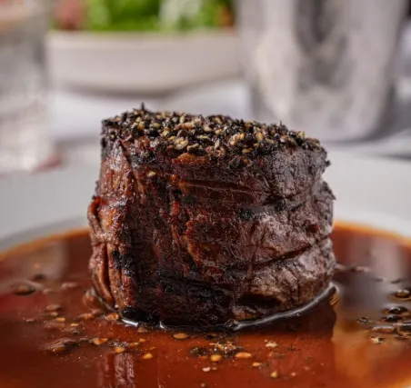 Corte de carne de res a la parrilla, servido sobre una salsa oscura y acompañado de especias.